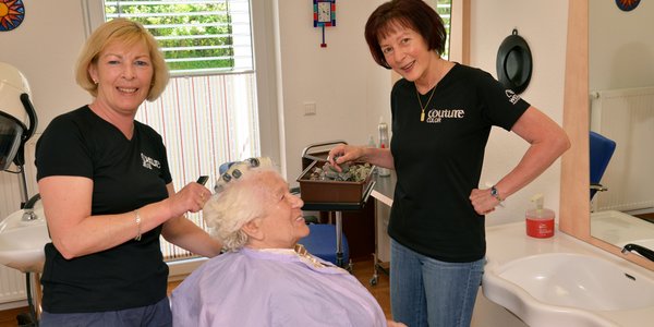 Zwei Friseure kümmern sich um die Haare einer Bewohnerin