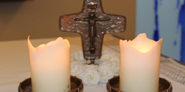 Zwei brennende Kerzen vor einem Kreuz 