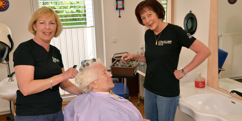 Zwei Friseure kümmern sich um die Haare einer Bewohnerin